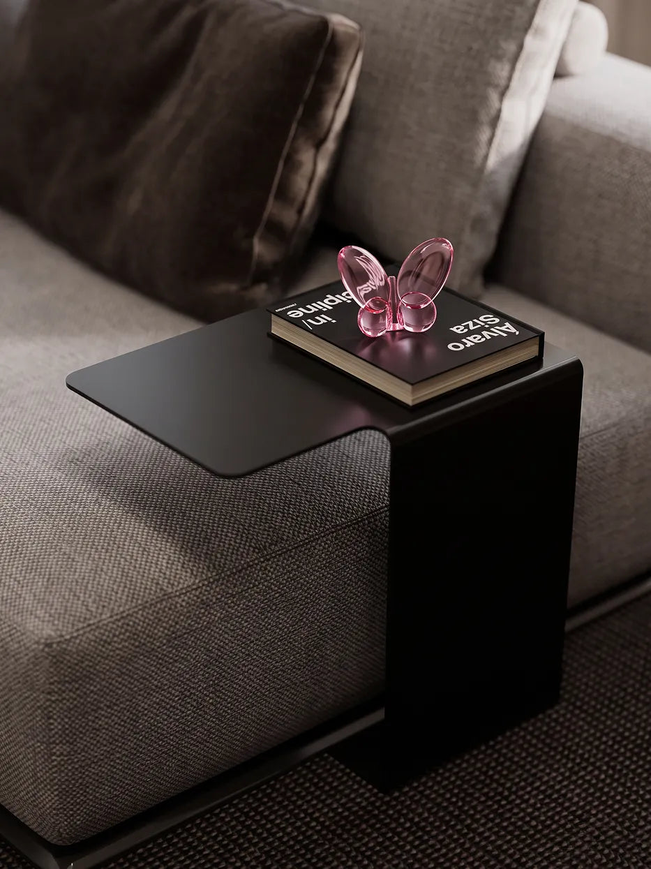 Official lifestyle image of the RESONG Butterfly Ornament - Pink, a sculptural pink glass butterfly ornament displayed on a side table in a modern living room.