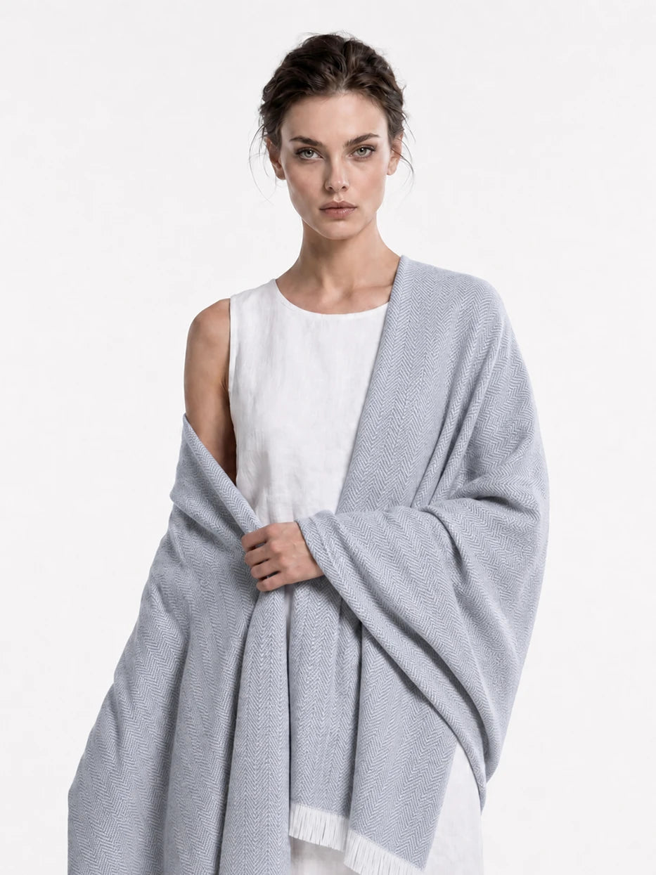 Minimalist close-up portrait shot of model wrapped with CHENZHI gray herringbone wool throw, fully displays complete full-width herringbone layout and bottom white fringe design, dual function as decorative home couch cover and wearable shawl for indoor & outdoor use