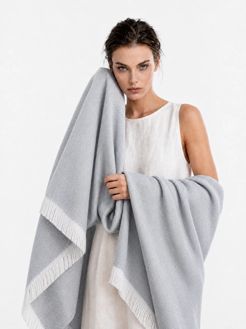Pure white background half portrait shot of model wrapped with CHENZHI gray herringbone wool blanket, demonstrates multi-scene usage as wearable shawl, office nap cover, outdoor beach wrap, lightweight silky breathable linen wool blend fabric suitable for all seasons, minimalist wearable home textile for daily rest and travel