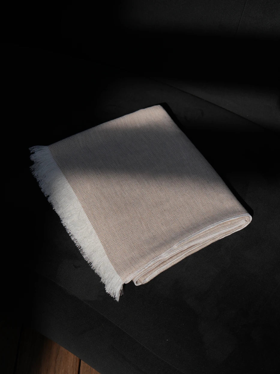 Minimalist interior still shot of folded CHENZHI herringbone wool throw placed on curved black accent armchair on solid wood flooring, warm high-contrast match between soft khaki textile and dark furniture, lightweight silky breathable blend fabric without bulky texture, great decor for entryway lounge, reading nook, hotel rest corner, modern dark tone interior matching