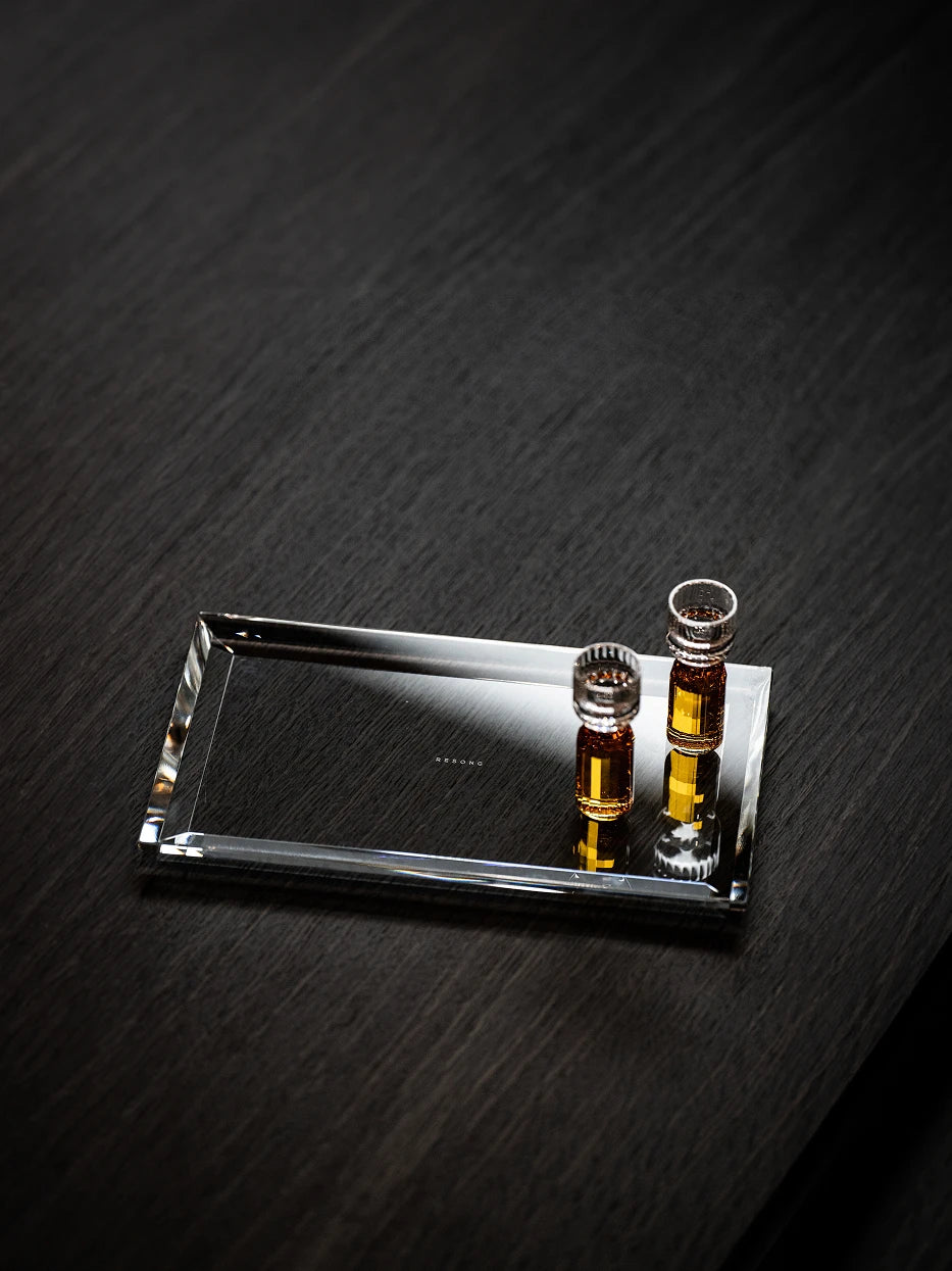 Luxury dark-toned vanity layout shot of crystal long tray holding essential oil bottles on dark wood dresser