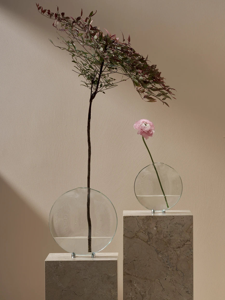 Wabi-sabi matching furnishing shot of large & medium Fishmouth vases with tall foliage and peony on travertine stone display plinth against warm beige wall
