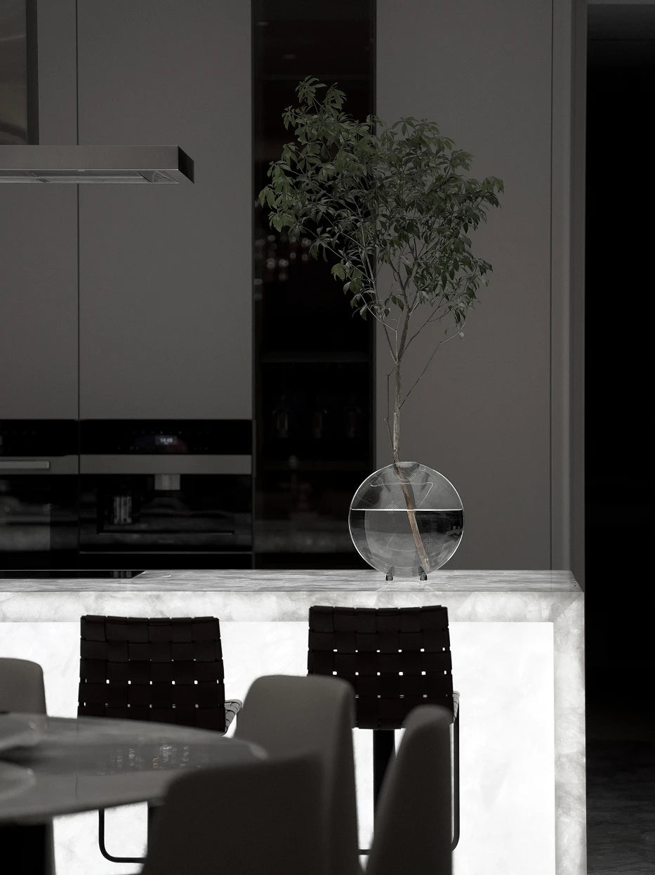 Monochrome minimalist kitchen furnishing shot of large Fishmouth vase with tall foliage on white marble cooking island