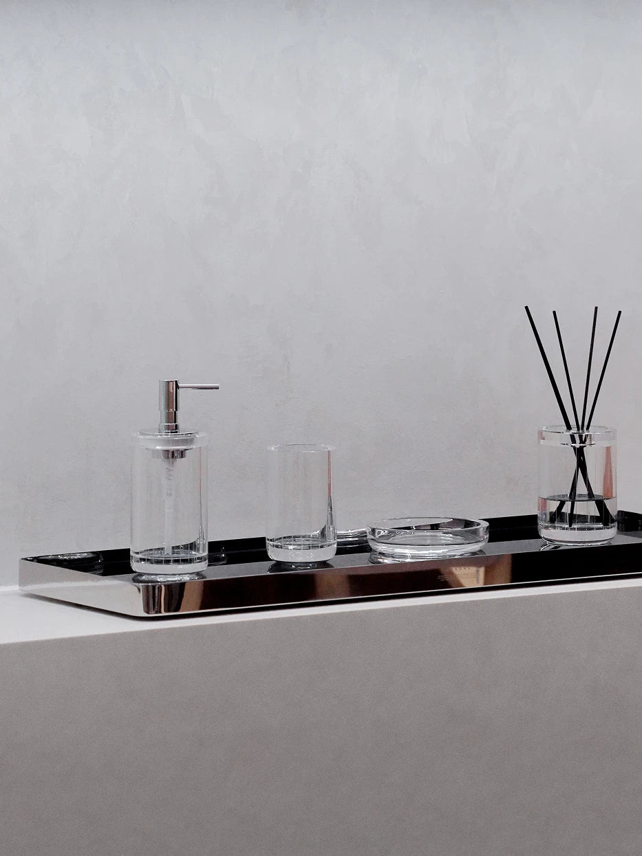 Minimalist bathroom vanity shot of lengthened HD black tray holding soap dispenser, tumblers and reed diffuser on light grey cement countertop