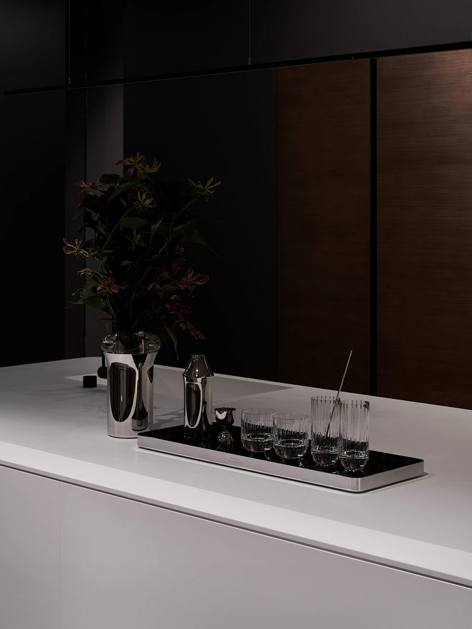 Minimal black & white kitchen layout shot of large HD black tray with metal vase and full set of striped glassware on pure white stone countertop
