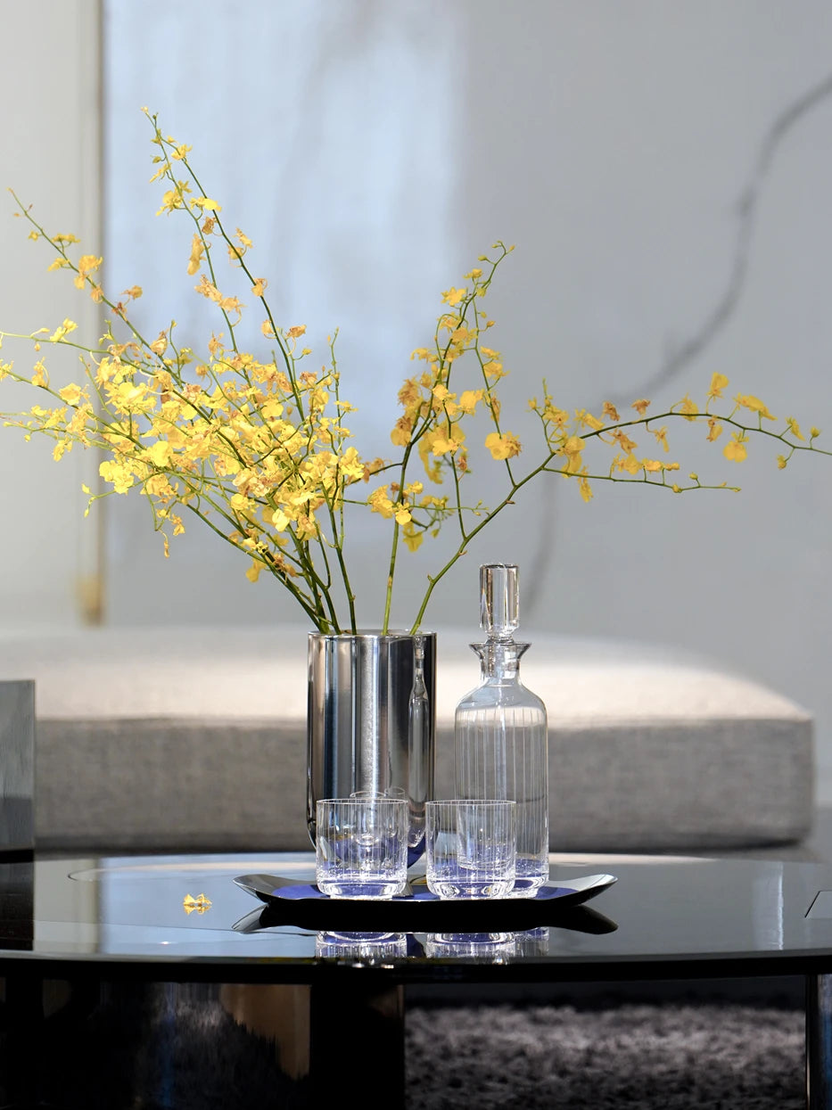 Minimal light luxury living room layout shot of HD S shallow handled tray holding striped glass cups beside golden orchid vase on black glass coffee table