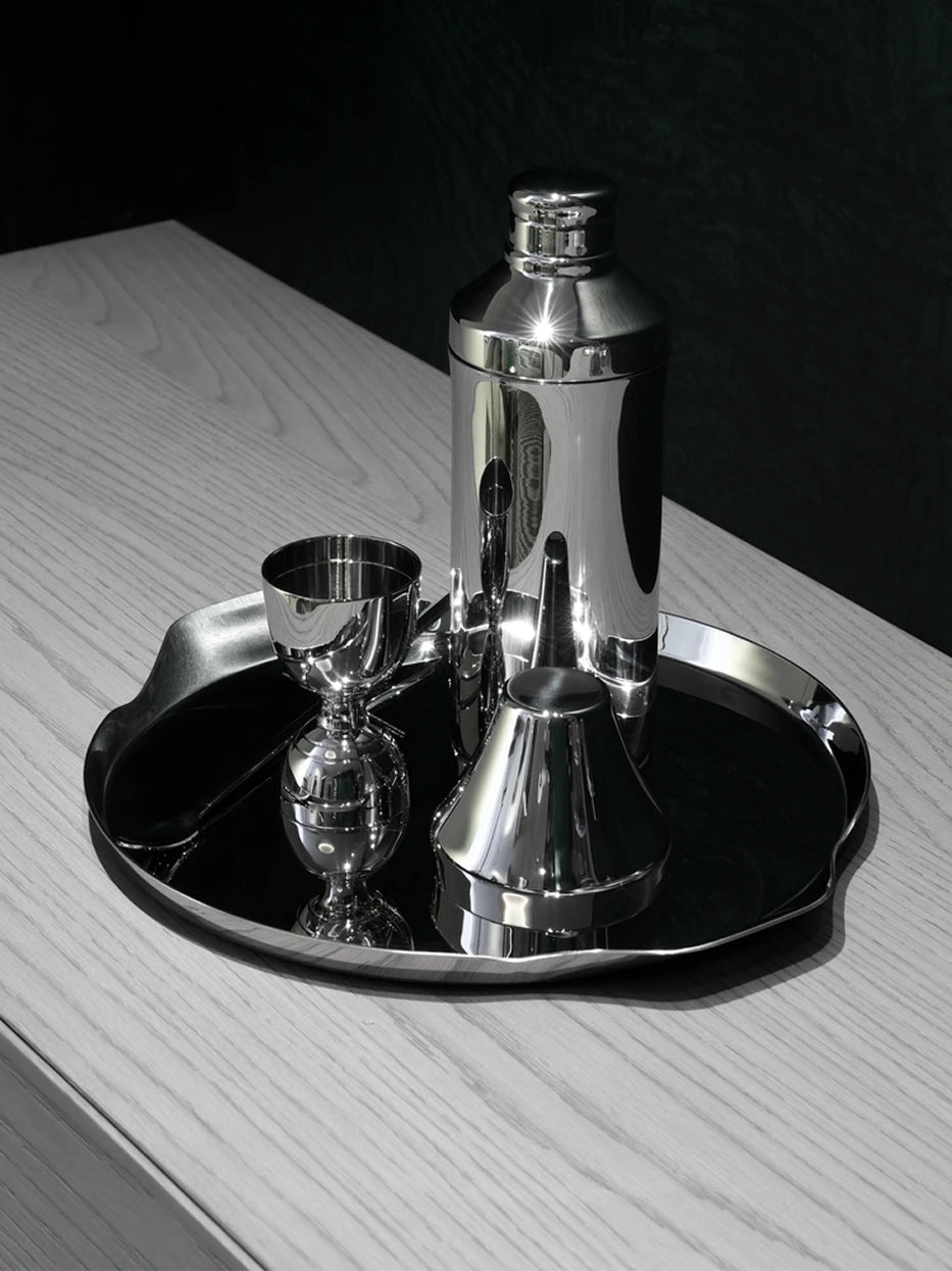 Dark tone bar still life shot of HD S handled tray full of stainless cocktail shaker set on light wood tabletop