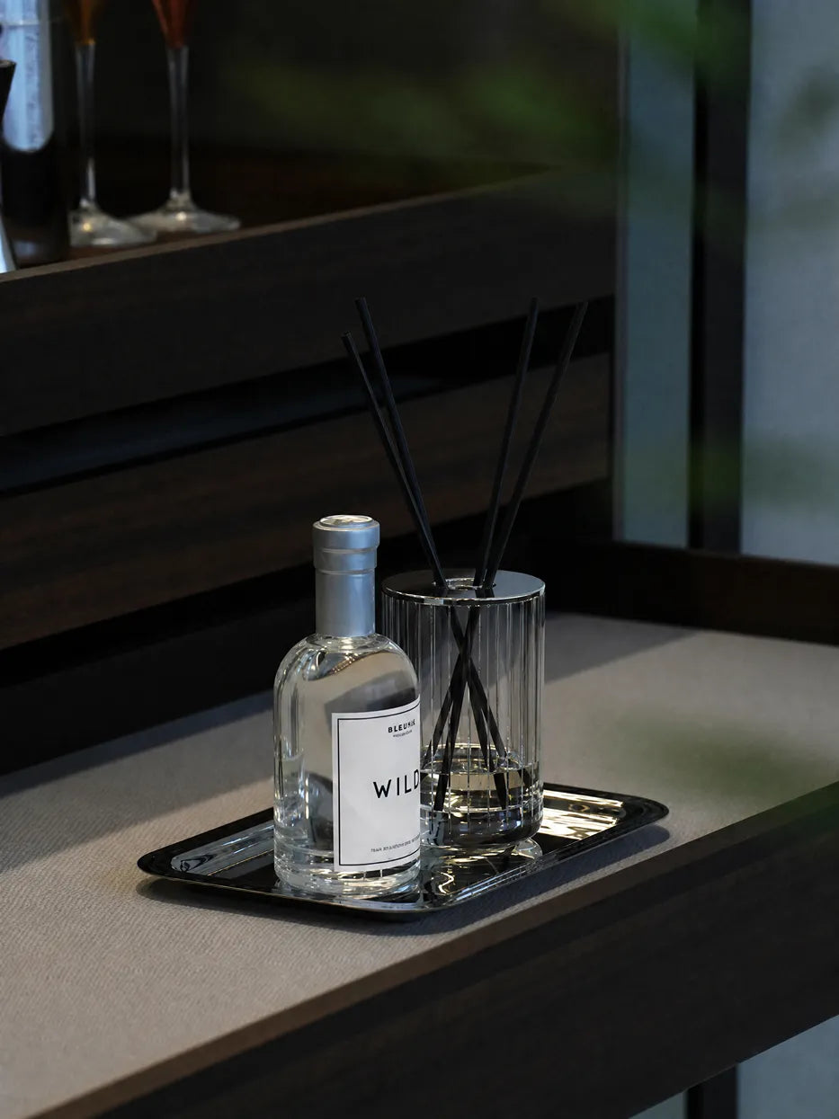 Minimal bedroom layout shot of HD small stainless steel tray holding reed diffuser bottle on wood nightstand