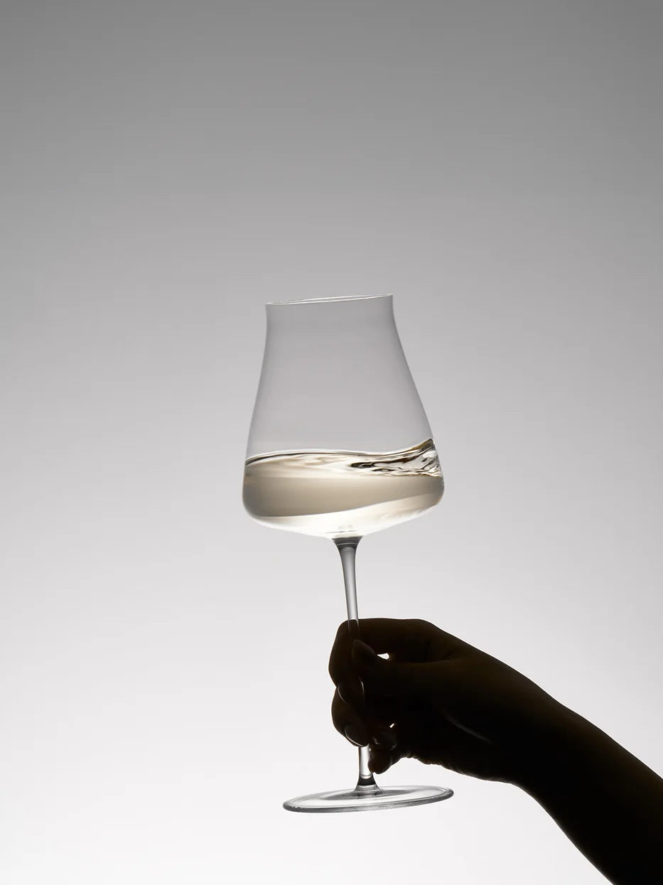 Minimal silhouette lifestyle shot of RESONG HOME 1833 slim crystal white wine goblet with white wine, hand swirling wine to release aroma, soft gradient grey background