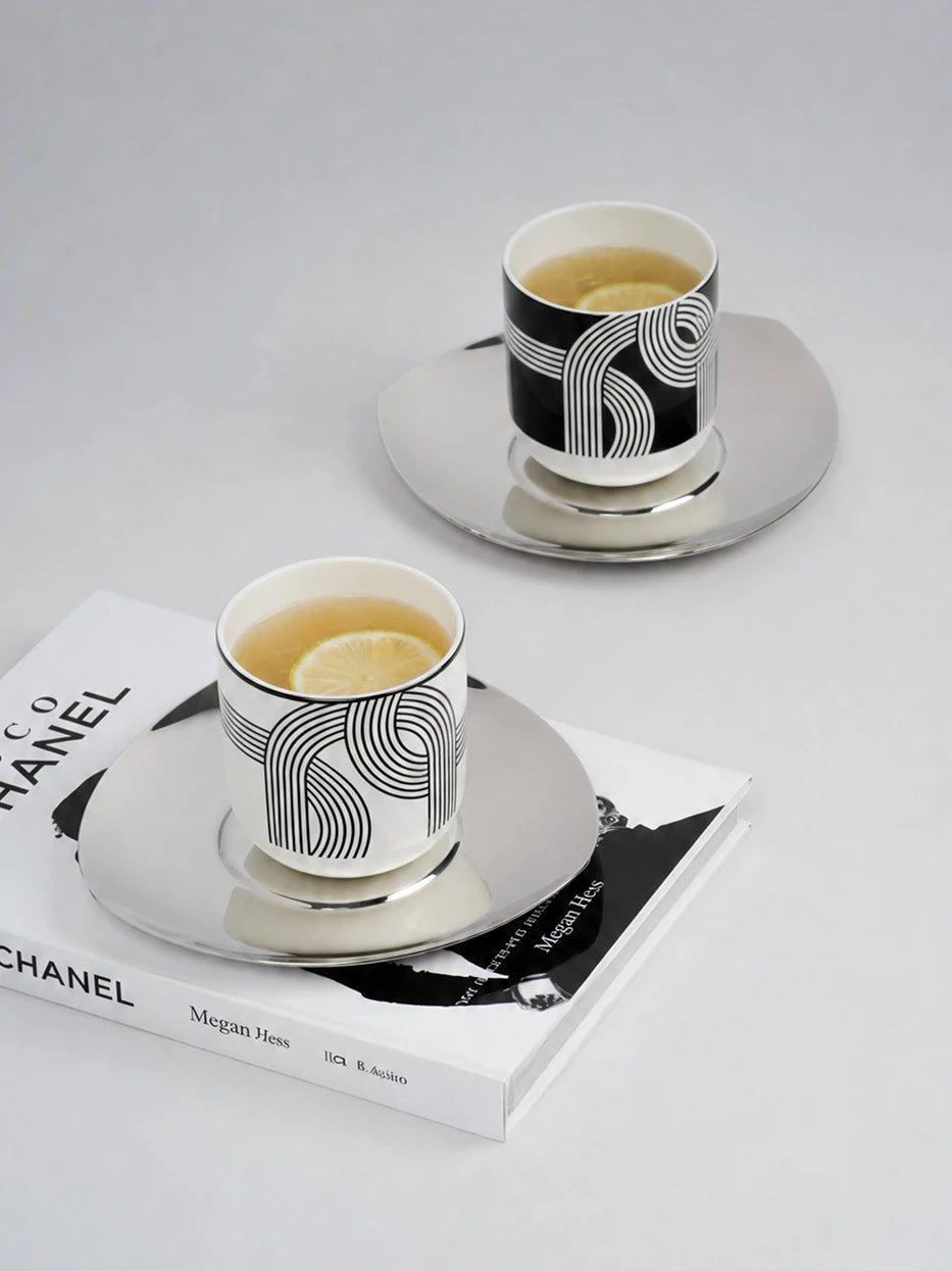 Artistic minimalist still life of ALK monochrome ceramic cups filled with lemon tea, laid on fashion hardcover magazine, smooth light grey studio tabletop
