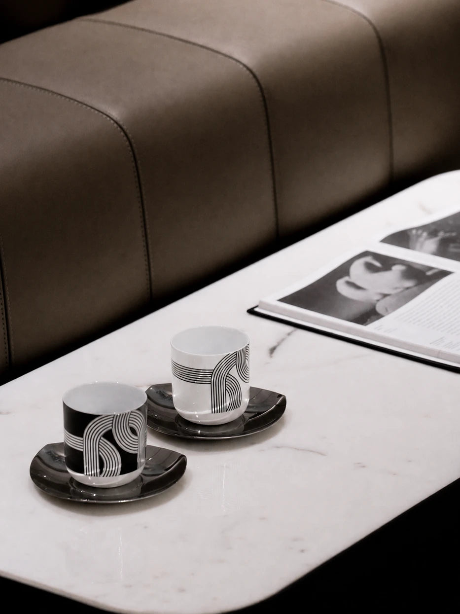 Luxury neutral tone lifestyle shot of ALK black & white geometric cup set on white marble long side table, brown leather upholstery and art magazine as decor