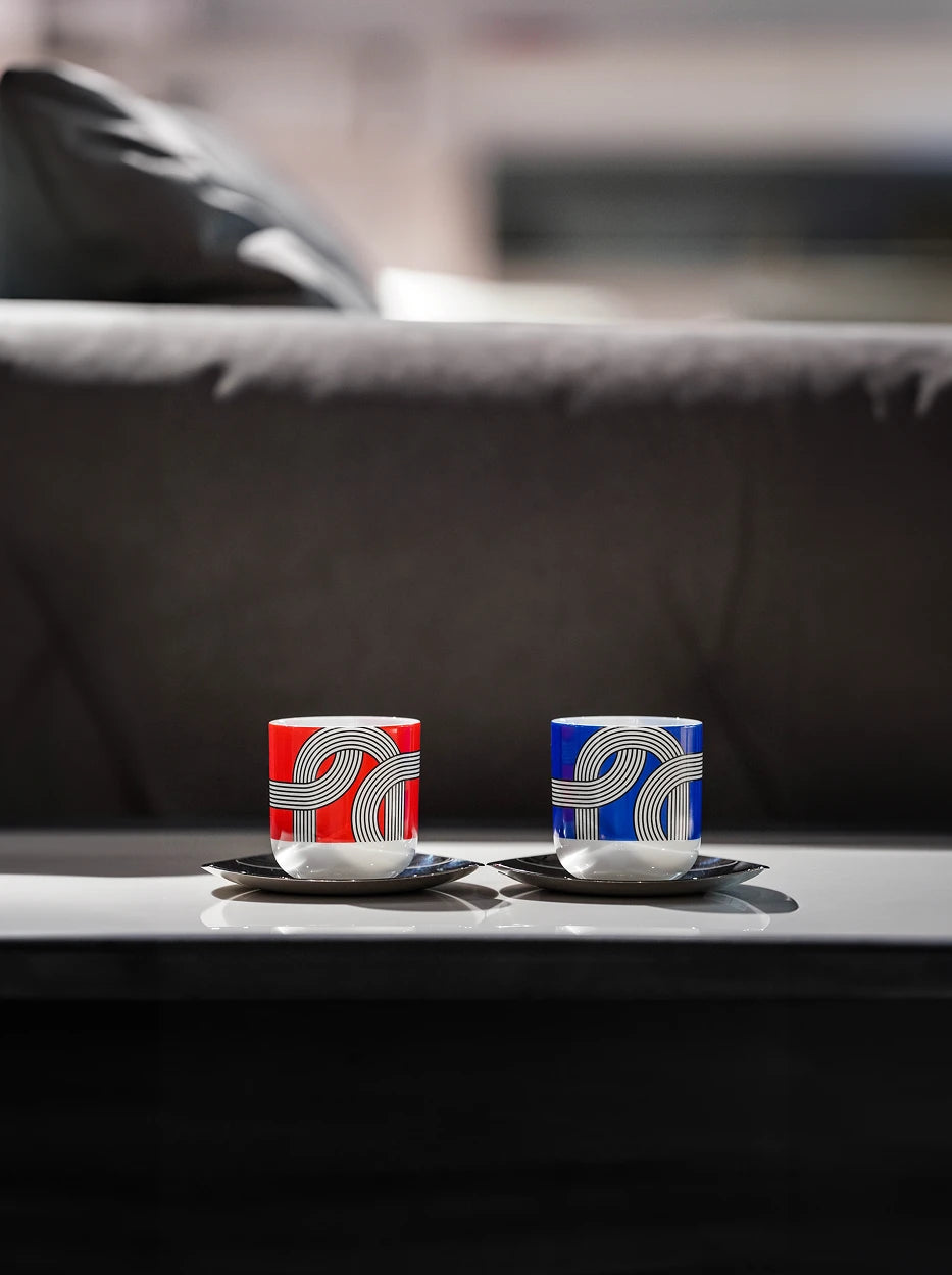 Cozy living room shot of ALK two-color ceramic cup set on reflective glossy coffee table, grey fabric sofa blurred as soft background