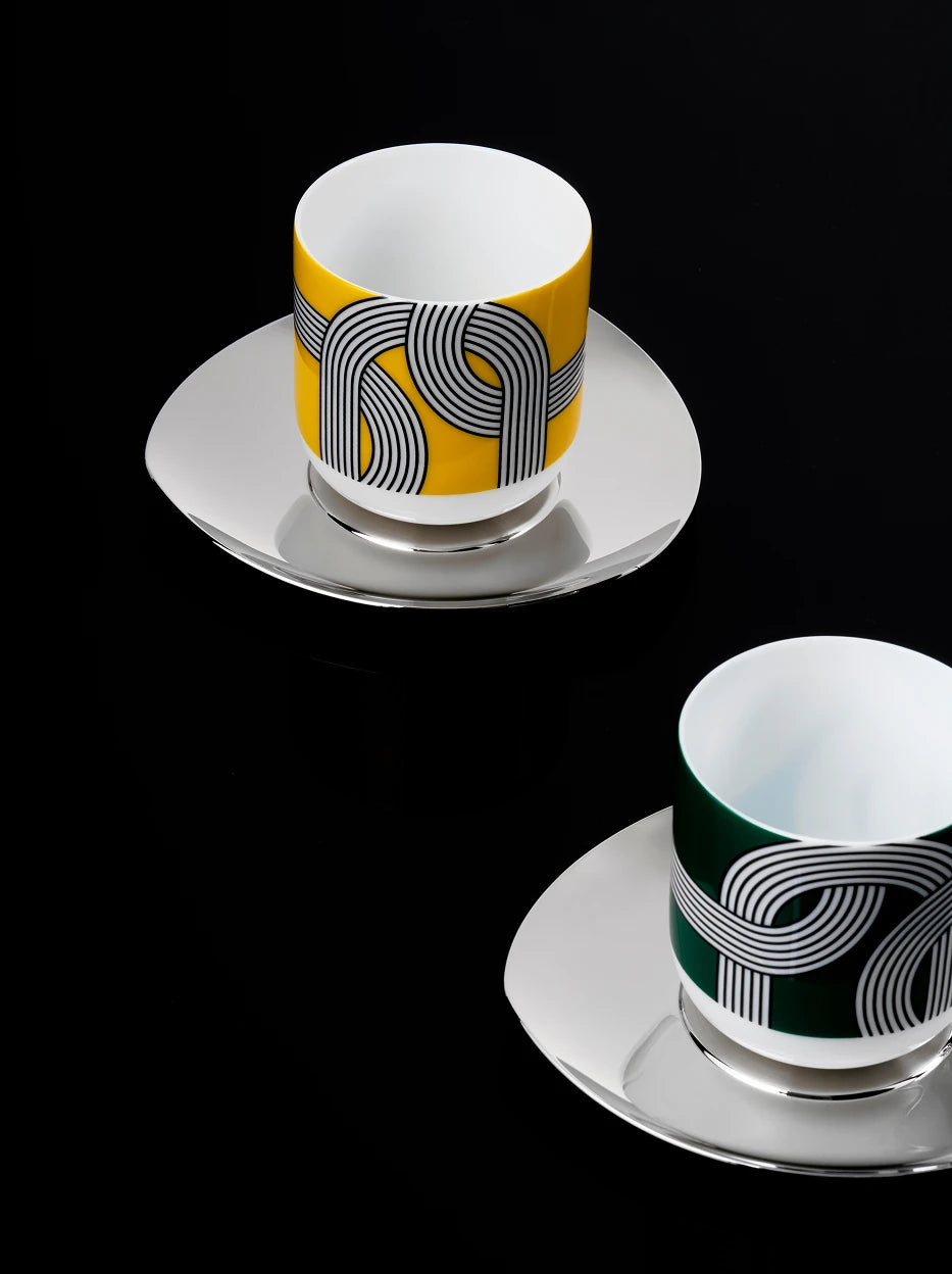 Dark tone minimalist close-up of two ALK geometric line ceramic cups with polished metal saucers, solid pure black background highlighting graphic print texture