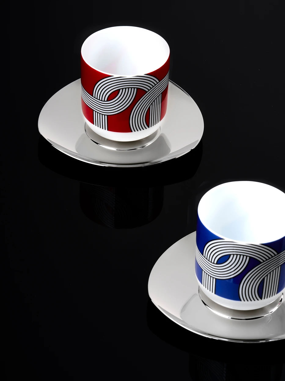 Dark minimalist close-up of two ALK geometric line ceramic cups with polished metal saucers, solid pure black background highlighting color contrast and graphic texture
