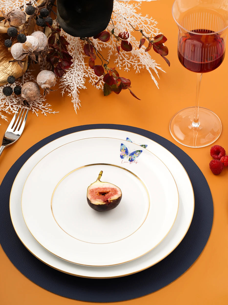 Warm orange table dinner layout shot of stacked butterfly gold-rim plates, matched with fig, raspberry, vertical striped wine glass and dried botanical decor