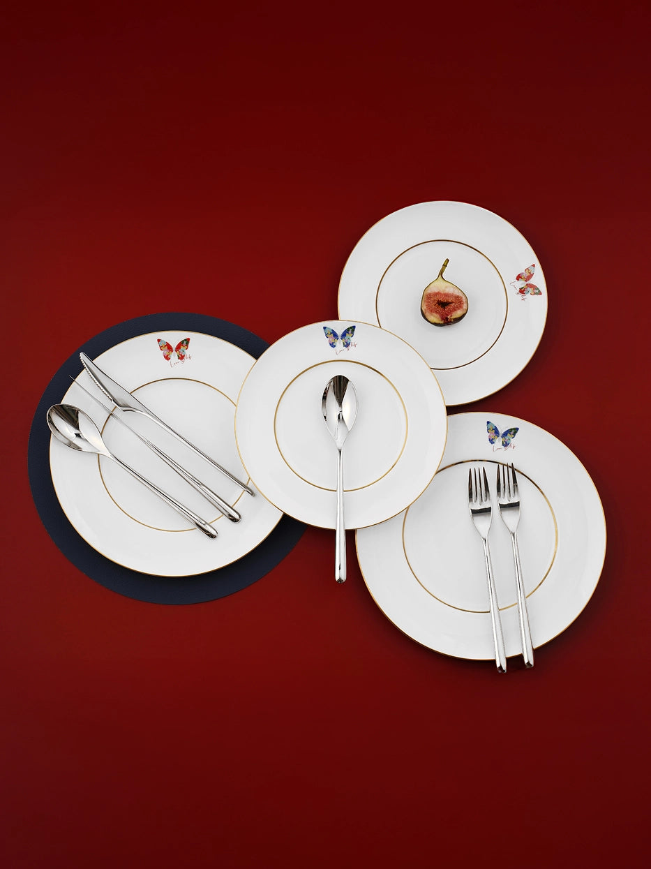 Minimal studio still life on solid red backdrop, assorted sizes of butterfly porcelain plates paired with complete stainless steel cutlery in staggered layout