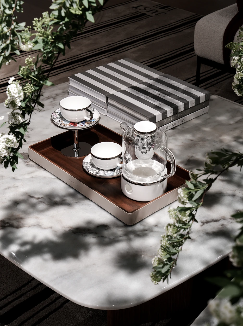 Elegant living room lifestyle shot of complete BUTTERFLY WHISPER tea set on leather wrapped wooden tray, decorated with fresh green foliage and stacked books on light marble tabletop