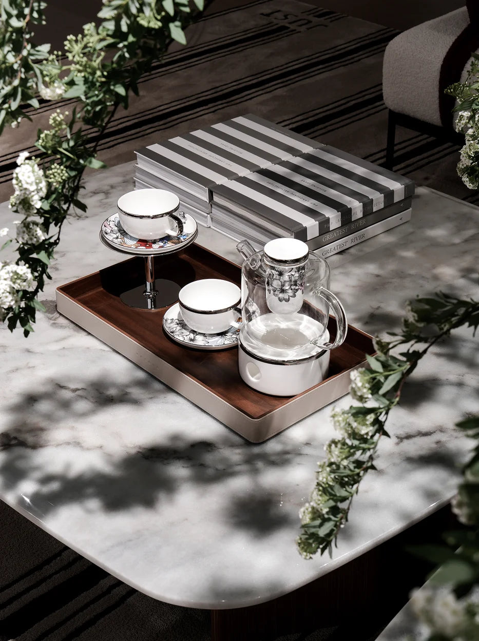 Elegant living room lifestyle shot of complete BUTTERFLY WHISPER tea set on leather wrapped wooden tray, decorated with fresh green foliage and stacked books on light marble tabletop