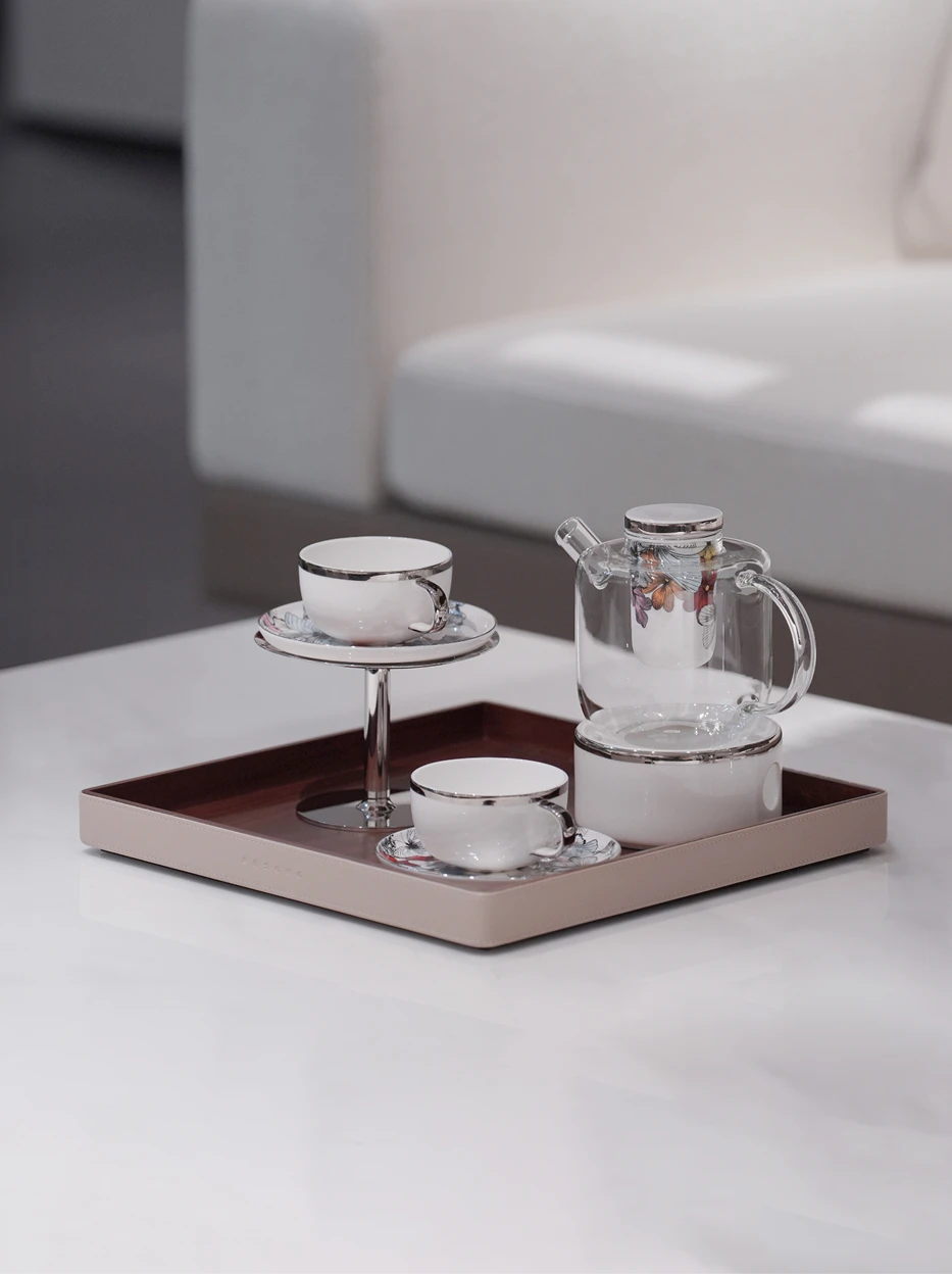 Minimal close-up studio shot of BUTTERFLY WHISPER full tea set neatly arranged on leather tray, soft light plain light table surface highlighting floral print details