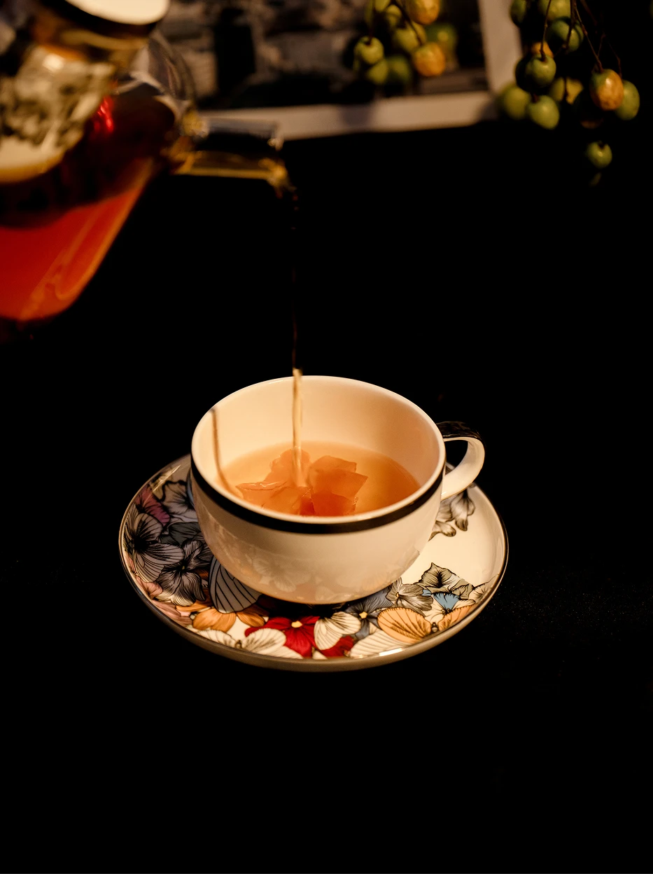Dynamic studio close-up of tea liquid pouring into BUTTERFLY WHISPER floral ceramic cup with dried flower inside, deep dark minimalist background