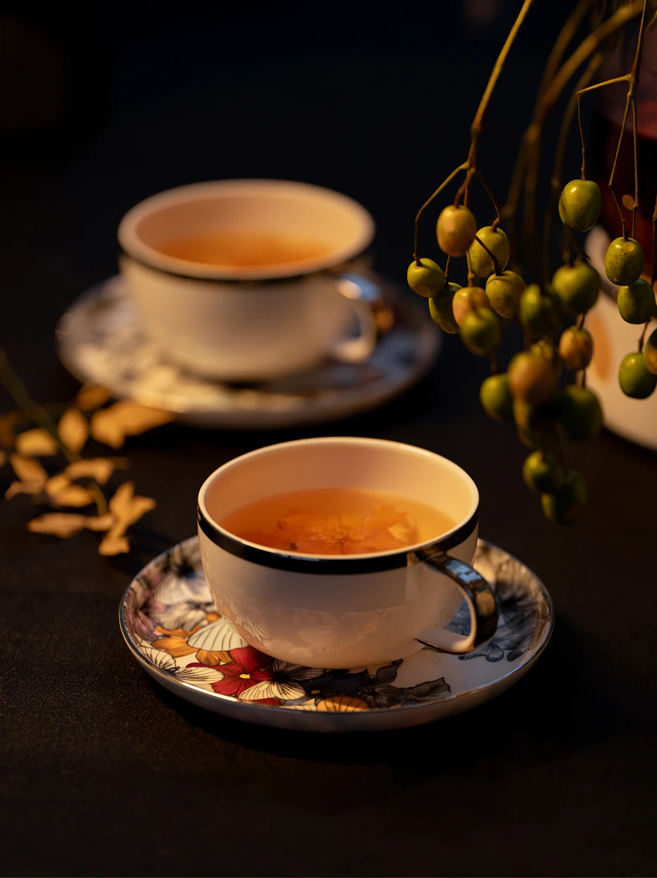 Warm dark cozy lifestyle shot of BUTTERFLY WHISPER ceramic tea set filled with blossom tea, decorated with natural berry branches on black matte tabletop