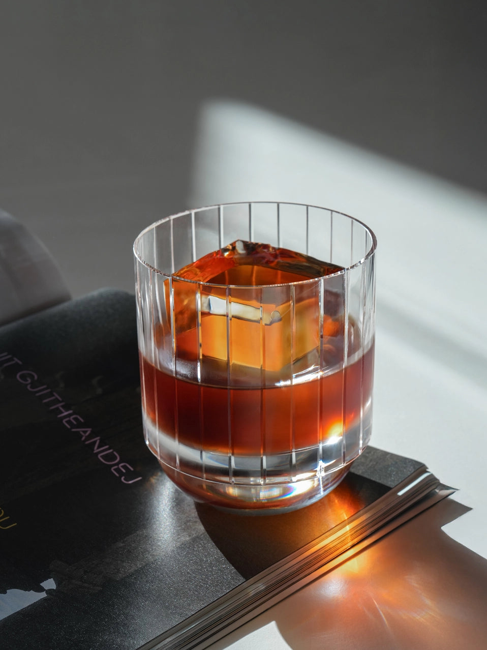Close-up detail of RESONG HOME DEWDROPS hand etched vertical ribbed crystal glass with whiskey and ice cube, weighted heavy base tumbler