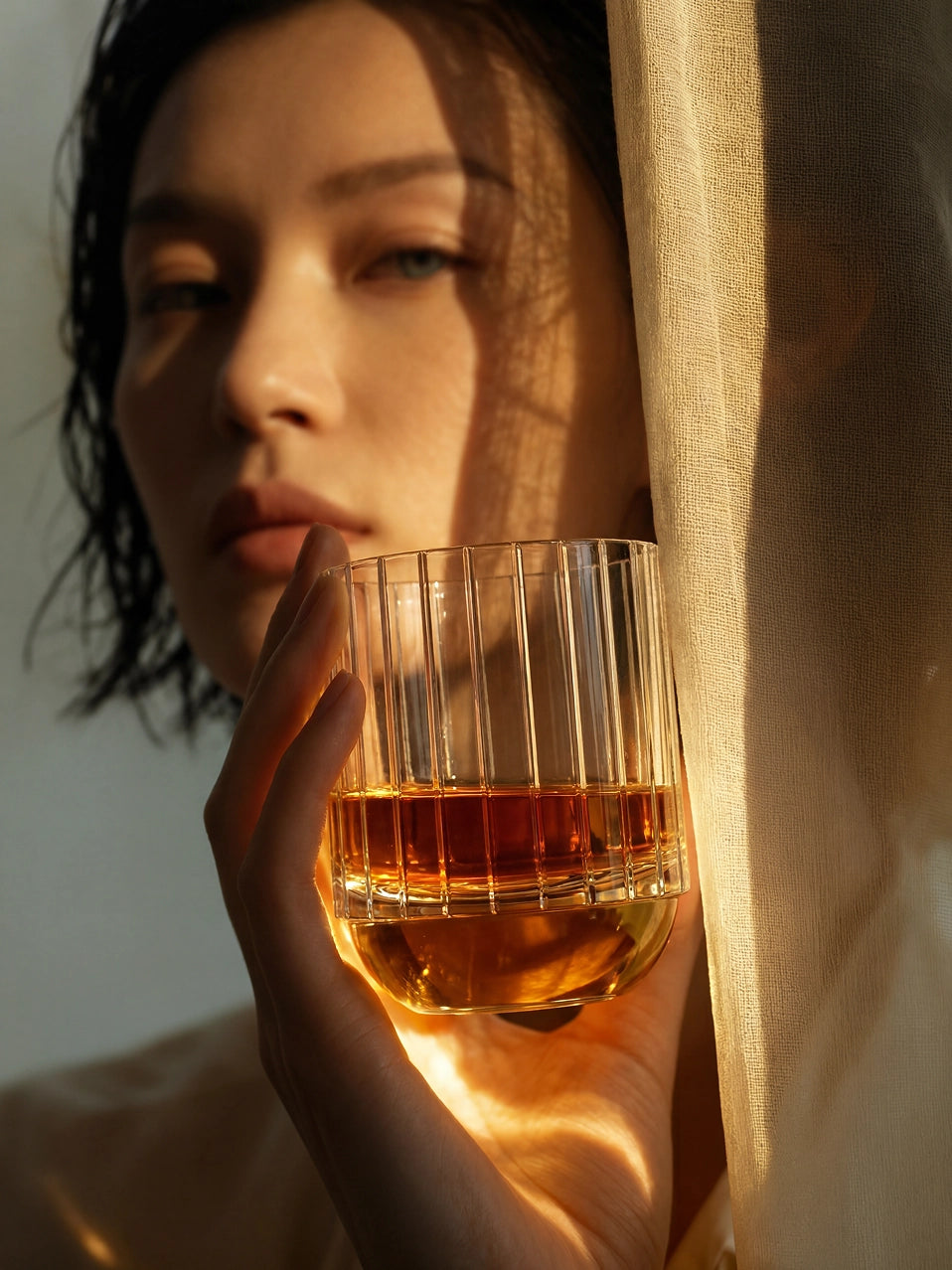 Woman holding RESONG HOME DEWDROPS dew drop textured crystal whiskey tumbler, warm light aesthetic luxury home bar tableware