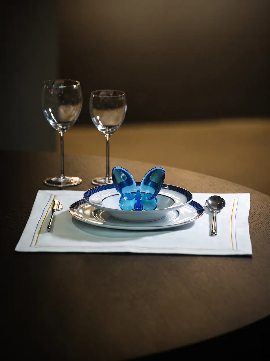 Atmospheric western dinner shot of ERYA blue rim plate set with wine goblets and metal cutlery on solid wood round table with soft warm lighting