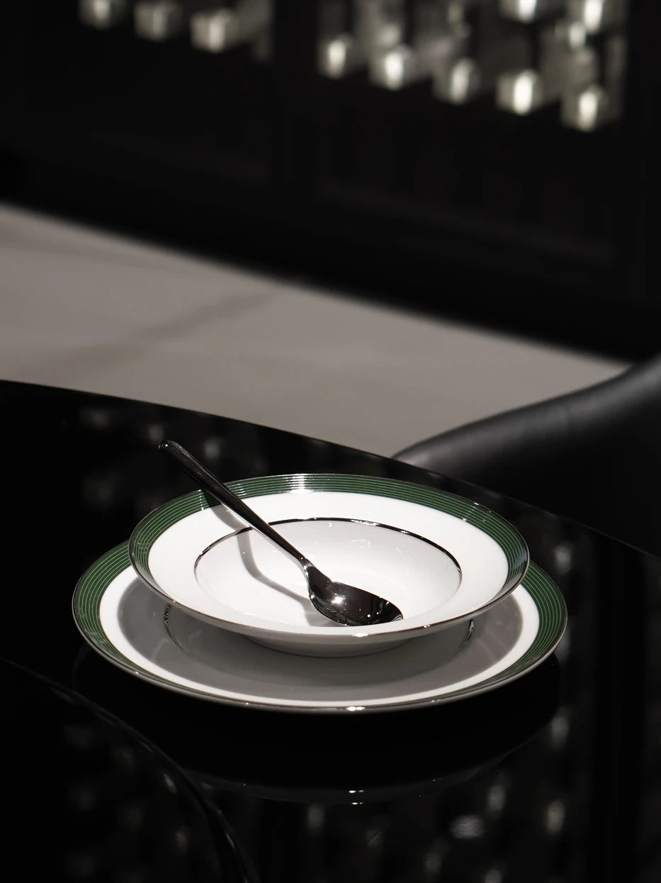 Dark minimalist close-up shot of ERYA large green rim plate set with metal soup spoon on reflective black round table