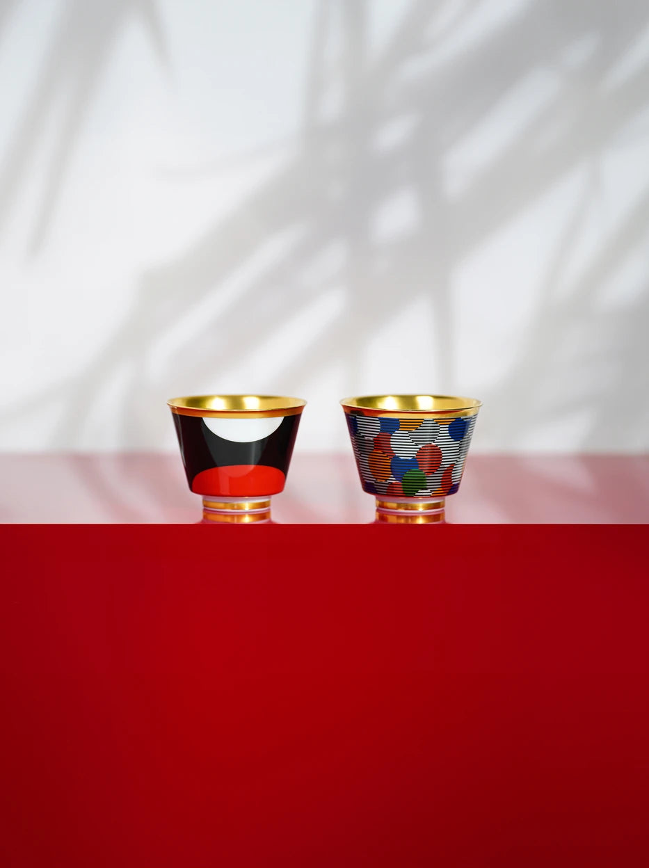 Artistic showroom display of the two GUOYUE gold-rim cups on layered red-grey glossy stand, palm leaf shadow on blank light wall to build soft layered texture