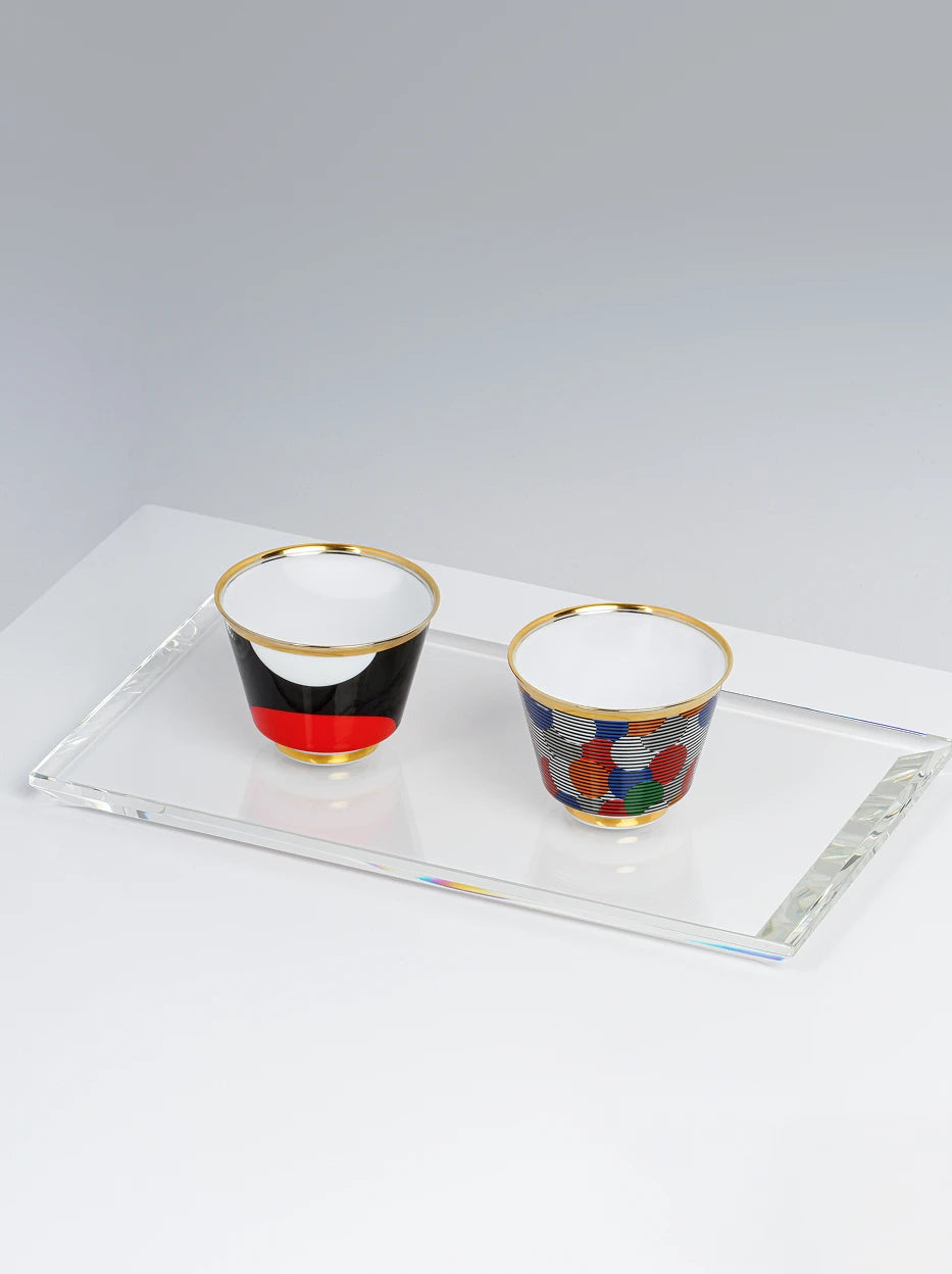 Minimal studio still life of Composition & Sunrise ceramic cups neatly placed on rectangular high-transparent crystal glass tray, smooth pure light grey tabletop with soft even lighting