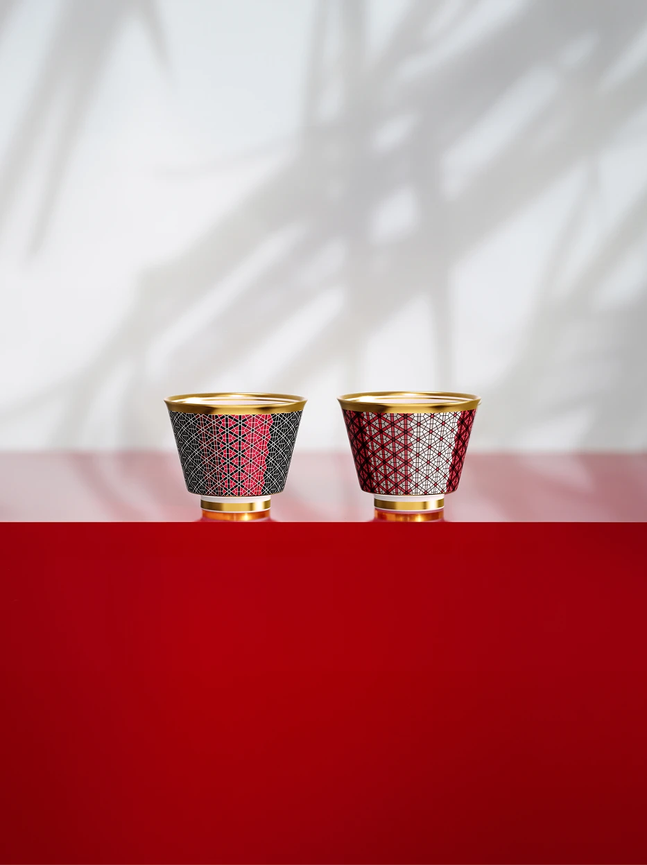 Minimal artistic display shot of two GUOYUE grid ceramic cups on layered red-grey glossy stand, palm leaf shadow on blank light wall for showroom display