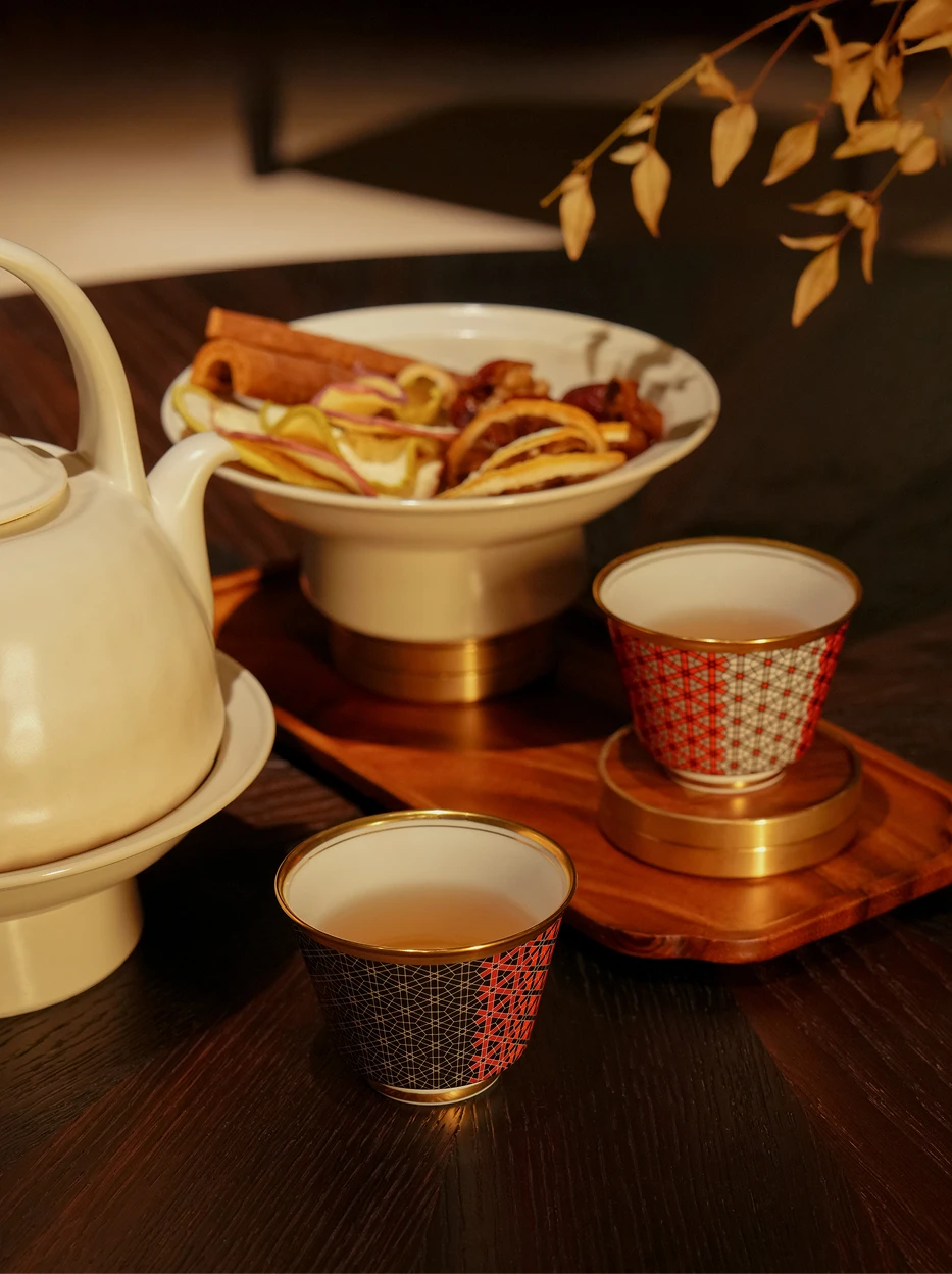 Warm Chinese-style tea room shot of two GUOYUE gold-rim grid cups on walnut tea tray, matched with white porcelain teapot and dried fruit tea accessories