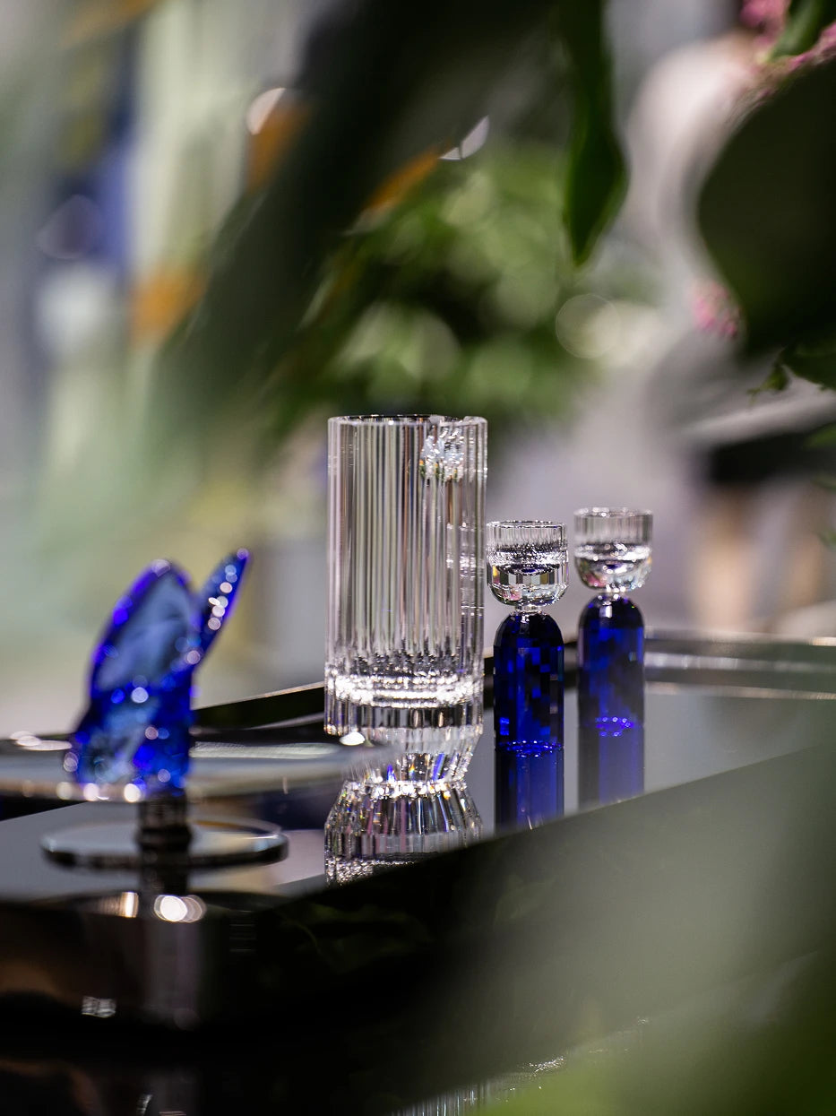Dark luxury lifestyle shot of HAOYING sapphire blue baijiu crystal set on reflective metal tray, blurred green foliage and bokeh light background
