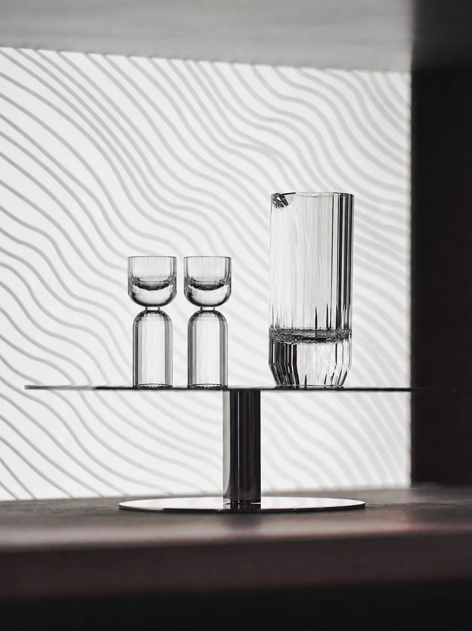 Modern minimalist lifestyle photo of HAOYING crystal baijiu serving set on sleek single-tier metal display stand, wavy textured white wall background