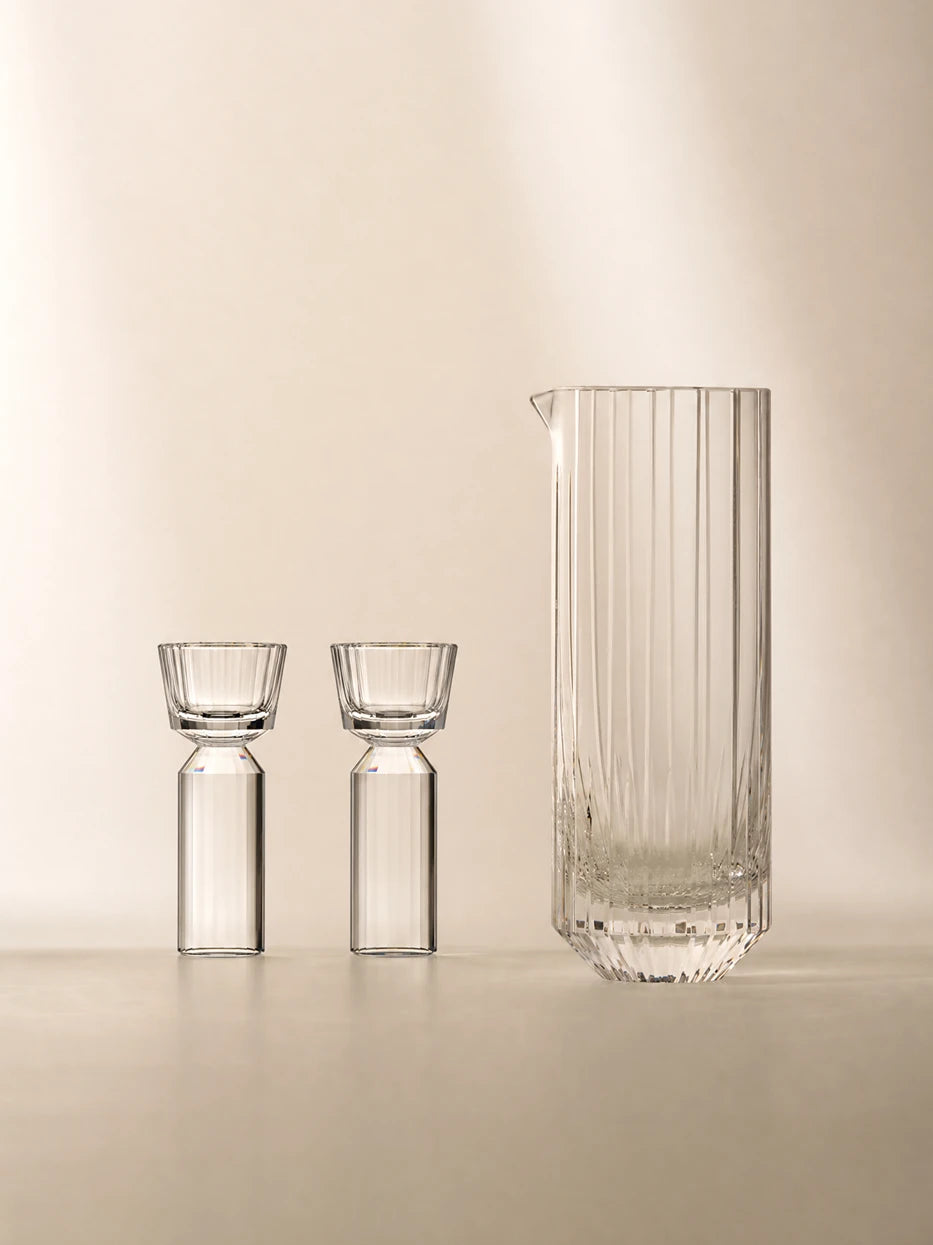 Soft warm minimalist studio shot of full HUAZUN clear crystal baijiu serving set, smooth beige background with soft side natural light highlighting vertical cut texture