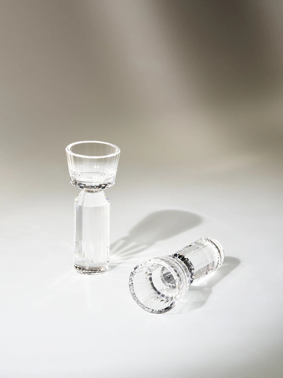 Minimal studio close-up of two HUAZUN faceted clear crystal shot glasses, gradient light grey background, natural sunlight casting striped refracted shadows