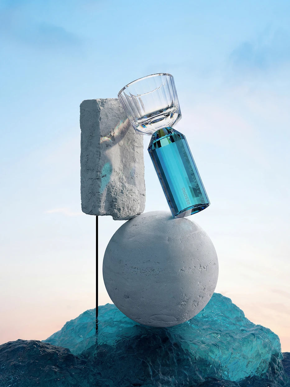Minimal conceptual studio close-up of single HUAZUN lake blue faceted shot glass, balanced on grey stone sphere above wavy blue water texture, soft sky blue backdrop