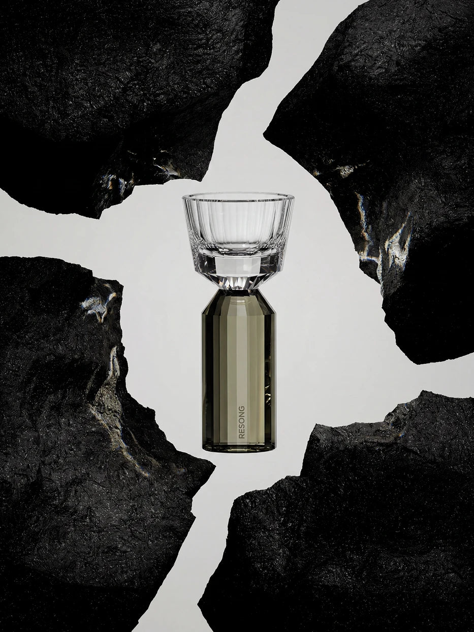 Sophisticated dark tone single product shot of HUAZUN smoke gray dual-body crystal shot glass placed on irregular rough black rock ornament, soft gradient gray backdrop
