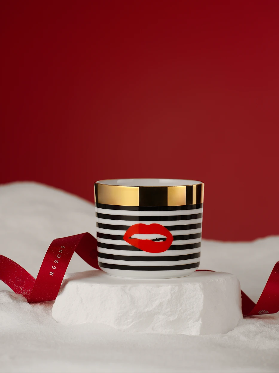 Festive gift still life of POP Art Red Lips gold-rim cup placed on artificial snow stone block, branded red ribbon and solid deep red backdrop for holiday display