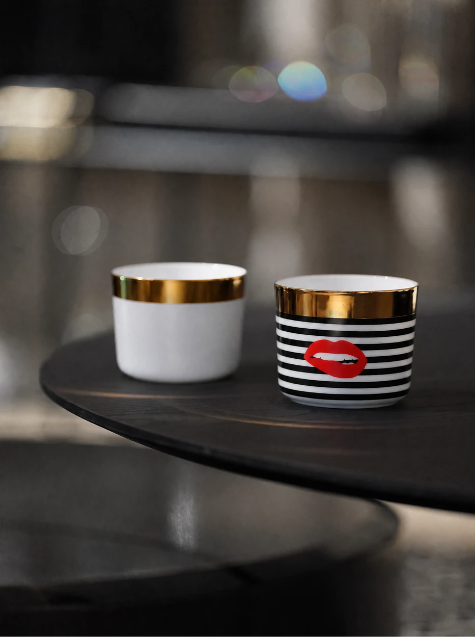 Atmospheric close-up shot of Silk White and Red Lips cups on curved dark wood coffee table, blurred bokeh light background
