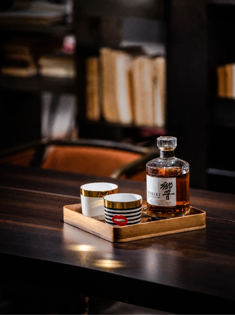 Wine tasting lifestyle shot of the two POP Art ceramic cups on walnut wood square tray, matched with whisky bottle in retro study space