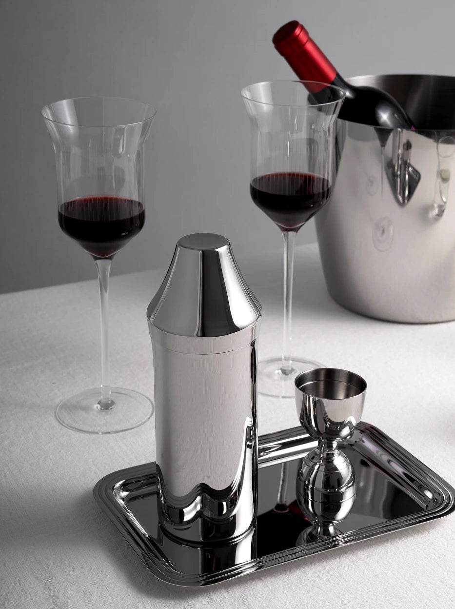 Atmospheric wine table still life of SHEDI stainless steel cocktail set paired with wine goblets and ice bucket on reflective metal tray, soft neutral fabric backdrop