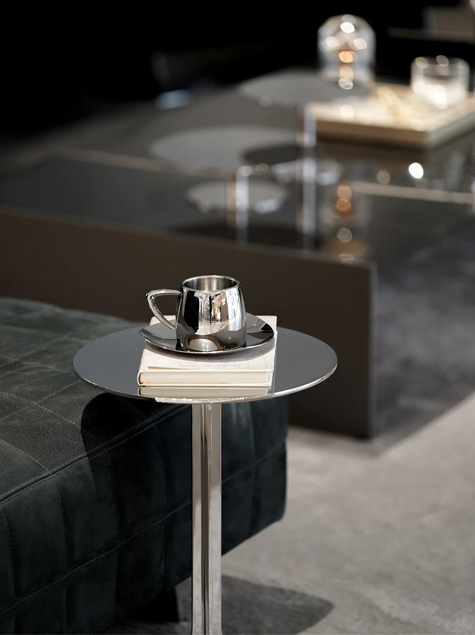 Light luxury living room shot of SHEDI large mirror steel cup & saucer placed on round metal side table, stacked art book and dark leather chaise as background decor