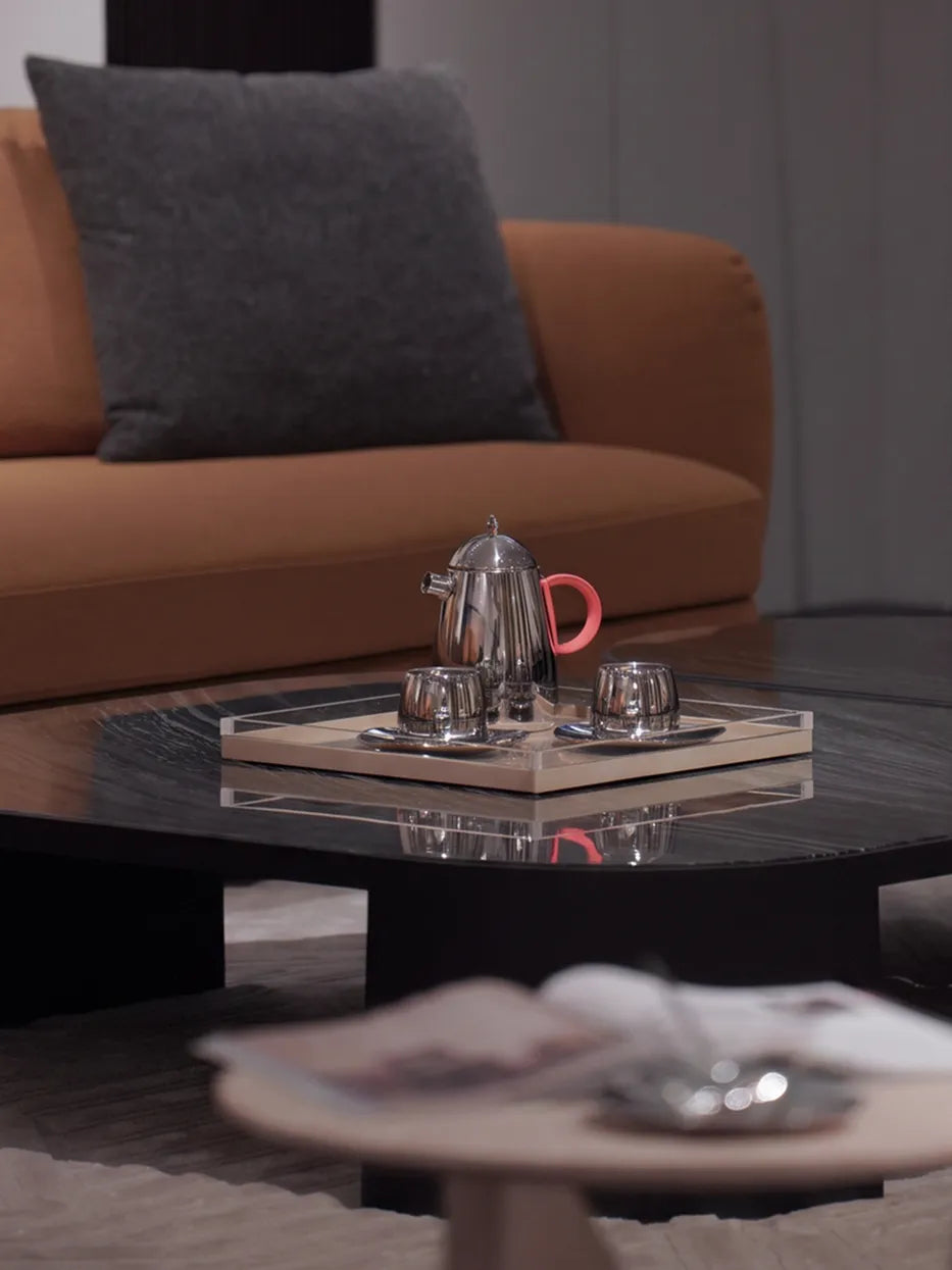 Full living room matching shot of large SHEDI teapot set on light leather tray, paired with silver vase and white rose flower arrangement on irregular black marble coffee table