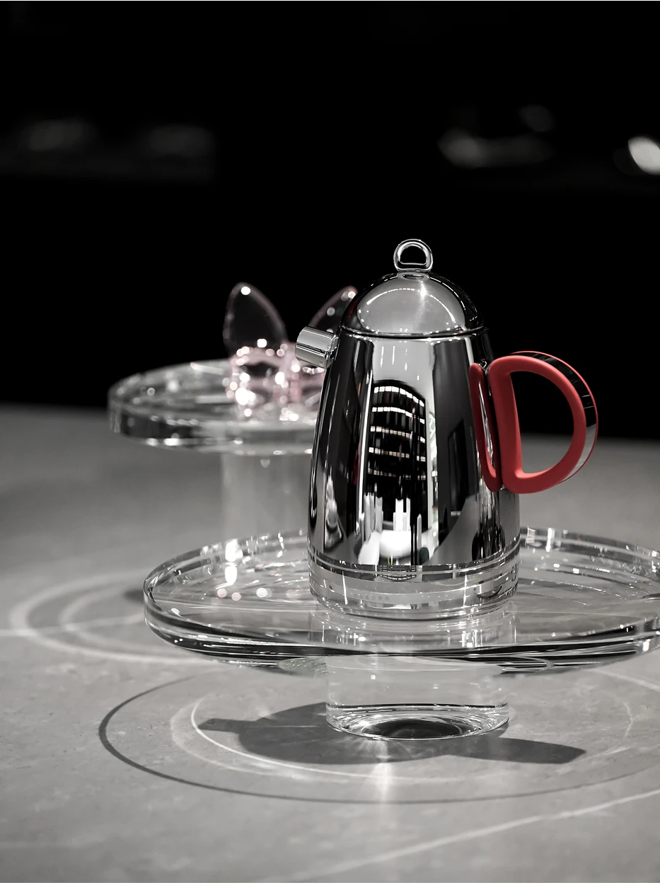 Light luxury showroom shot of SHEDI red handle small teapot placed on two-layer high-transparent acrylic display stand, minimalist grey interior with soft reflective texture