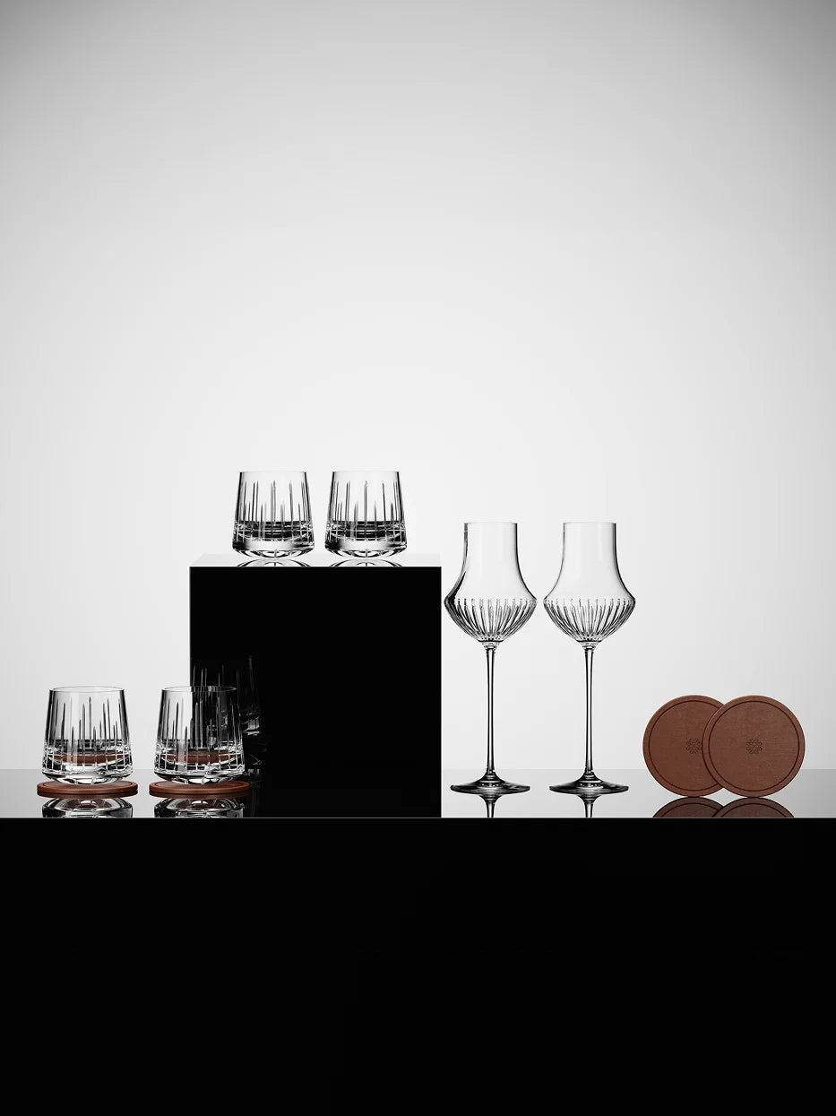 Minimal studio layered display of RESONG TRIUMPH crystal glass collection on black geometric platform, complete with matching round leather coasters, light grey reflective background