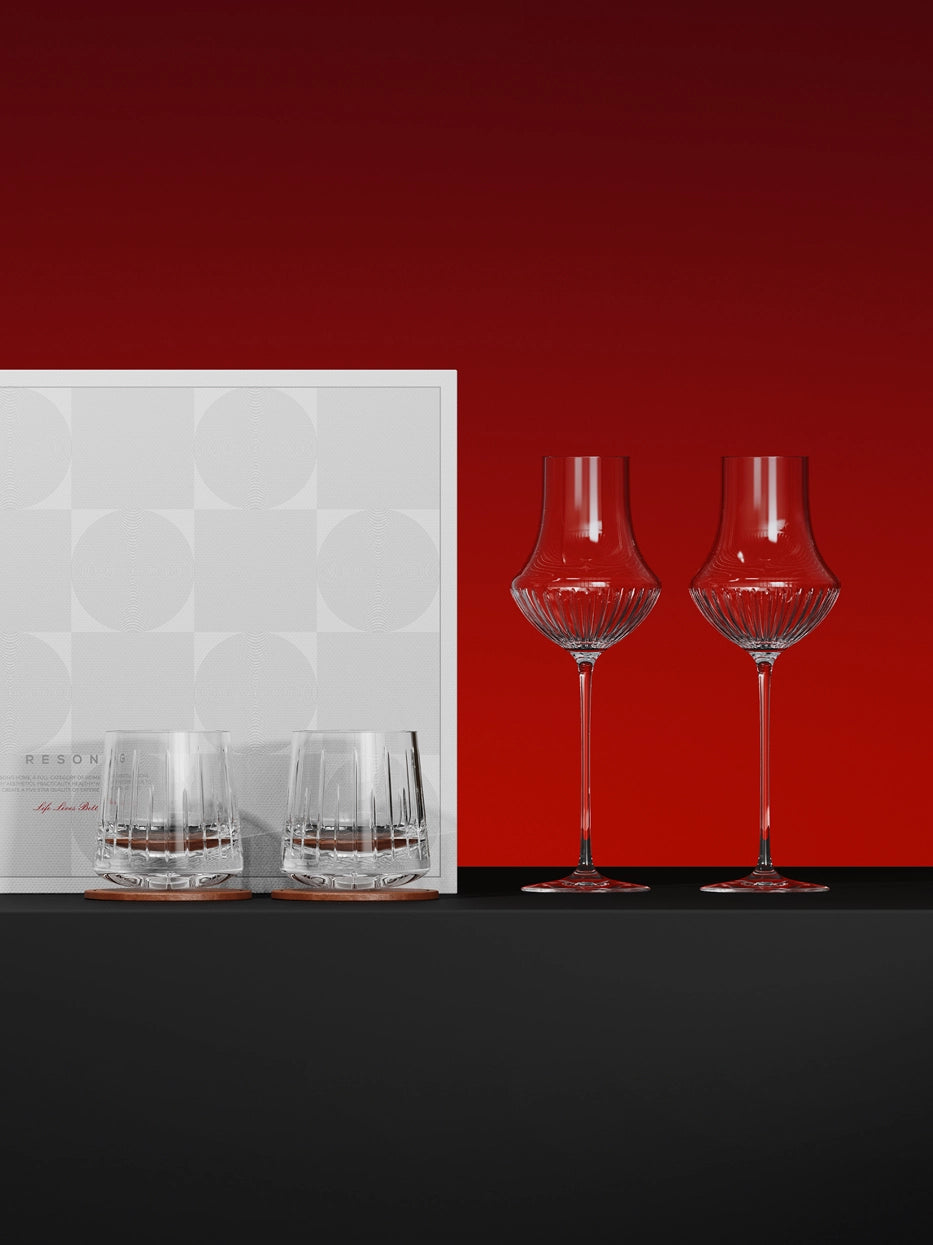 Luxury studio gift display of RESONG TRIUMPH wine & whiskey glass set with original gift box, solid deep red background, reflective black tabletop