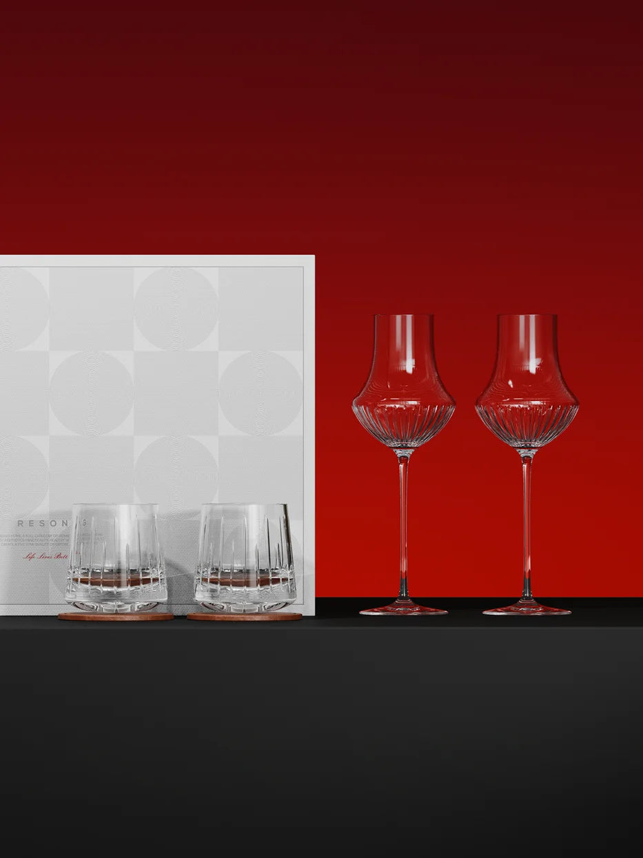 Luxury studio gift display of RESONG TRIUMPH wine & whiskey glass set with original gift box, solid deep red background, reflective black tabletop