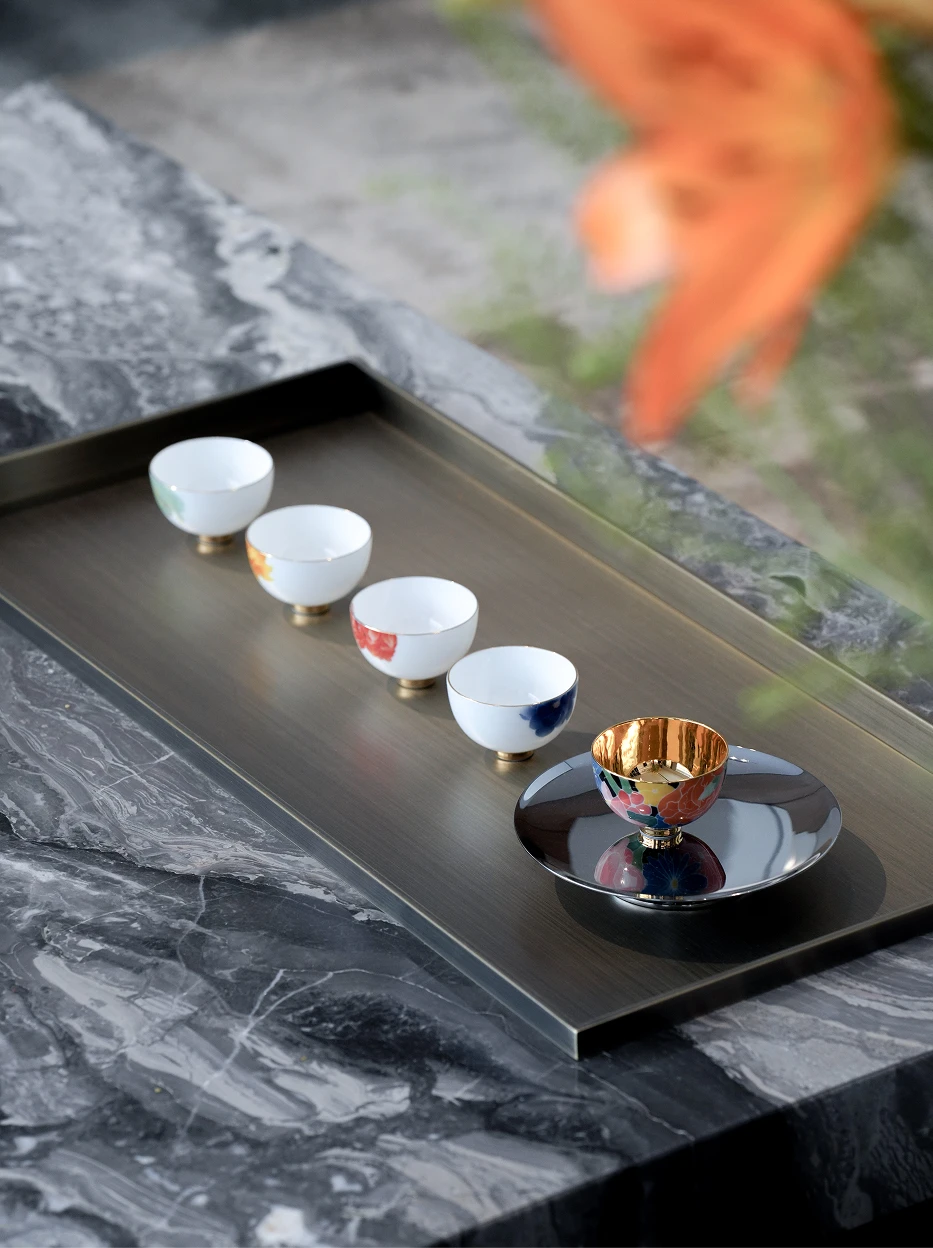 New Chinese-style tea room lifestyle shot of the five floral tea cups neatly arranged on rectangular metal tea tray, white marble tabletop with blurred orange foliage foreground